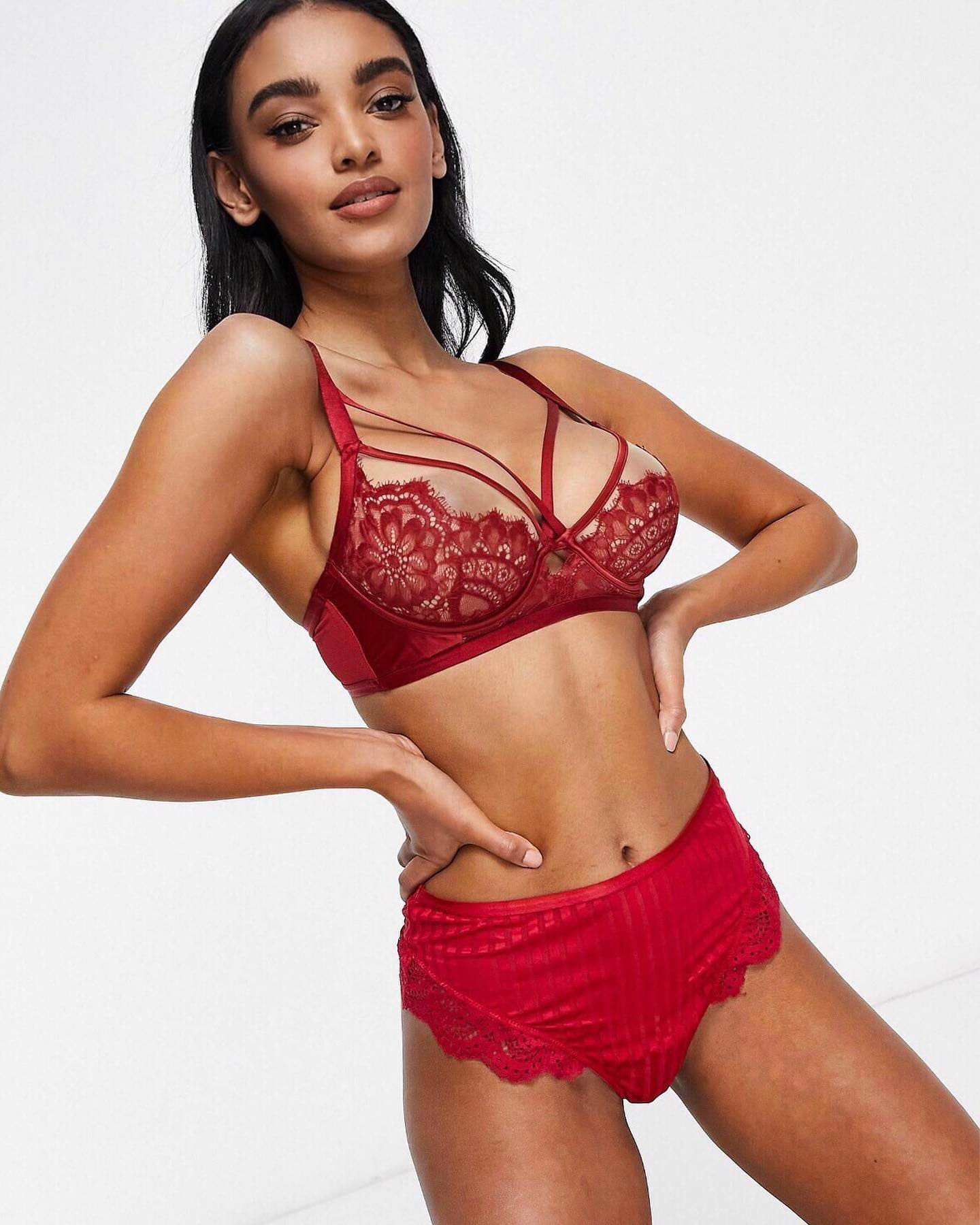 Anabel stands with hands on hips against a white background, wearing a red lace bralette and matching briefs.